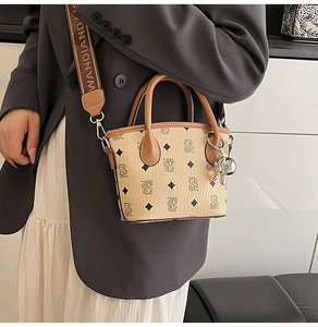Détail d'un sac seau beige avec large bandoulière tissée et pendentif ours