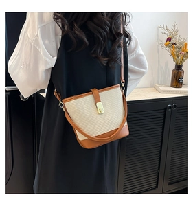 Detail of beige woven bucket bag with brown leather trim and golden metal turn-lock
