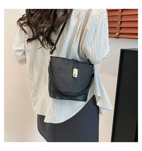 Detail showing the black woven bucket bag texture with gold hardware on model shoulder