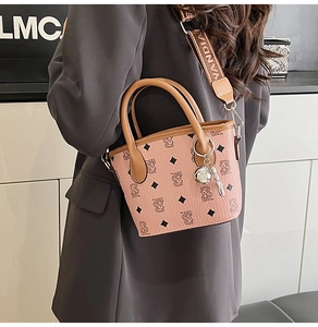 Détail d'un sac seau rose avec motifs d'ours, large bandoulière et pendentif argenté