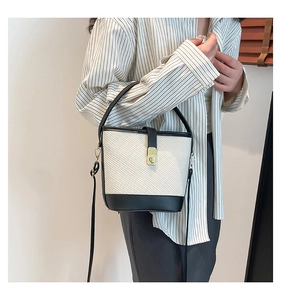 Détail du sac seau en paille tressée avec bordure en cuir noir et fermoir doré