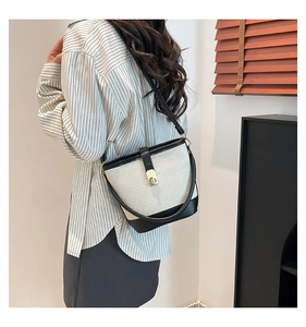 Detail of woven bucket bag with black leather trim and golden metal lock clasp