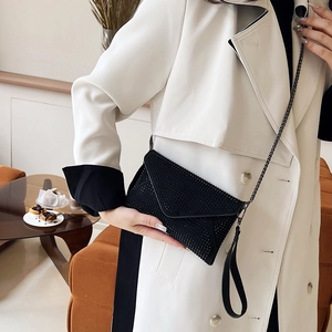 Pochette enveloppe noire en strass avec chaîne en métal portée par un mannequin