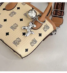 Détail du sac seau en cuir beige avec logo imprimé, bandoulière et breloque chien ballon