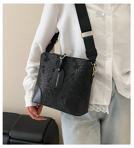 Close-up of black snake embossed bucket bag with wide fabric strap and gold hardware