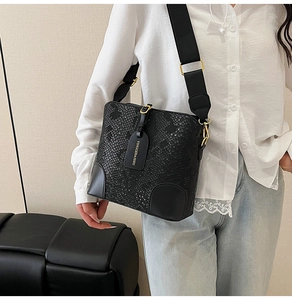 Detail of black snake-embossed leather bucket bag with wide strap and gold hardware