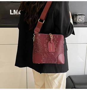 Detailed side view of burgundy snake-pattern bucket bag with wide strap and metallic studs