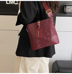 Detail of burgundy bucket bag with snake-embossed texture and wide fabric shoulder strap