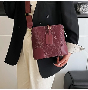 Detail of burgundy snakeskin bucket bag with wide fabric strap on a model outfit