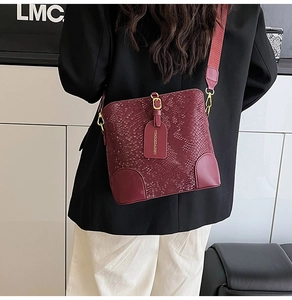 Detail of burgundy snakeskin texture bucket bag with wide strap and gold hardware