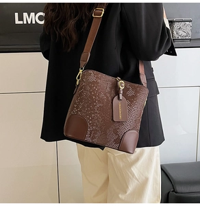 Detail of snake-embossed brown bucket bag with wide canvas strap and leather reinforcement