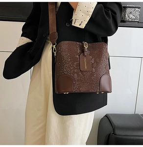 Close-up of brown faux snakeskin bucket bag with wide shoulder strap and brand tag