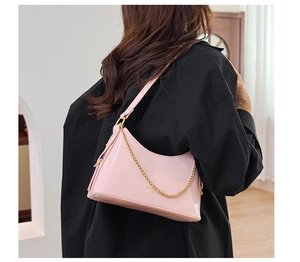 Detail of pink patent leather hobo bag featuring gold chain and shoulder strap on model