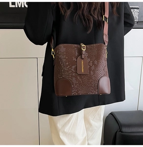 Detail of dark brown snakeskin bucket bag with wide strap on a model in professional outfit