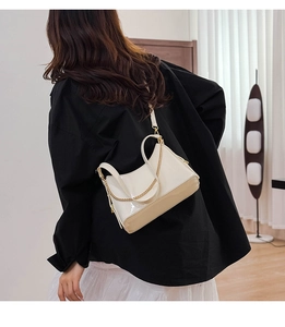 Beige patent leather bucket bag with gold chain strap shown on model in a modern room