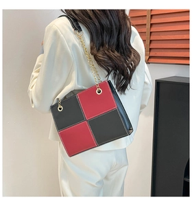 Detail of red and black square shoulder bag with gold chain strap on a model