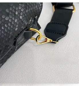 Detail of gold metal hook and wide fabric strap on black snakeskin bucket bag