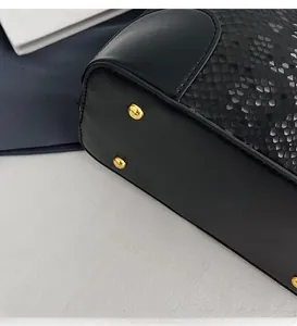 Close-up of black leather bucket bag bottom with golden metal feet and snake texture