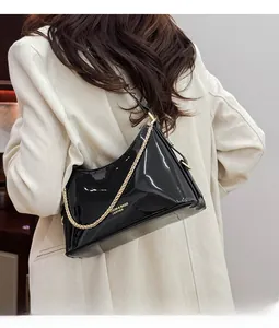 Detail of black patent leather underarm bag with gold chain strap on a model