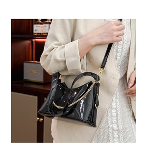 Close-up of black patent leather handbag with gold chain detail on beige blazer