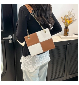 Detail of a brown and white checkered crossbody bag with gold chain strap detail