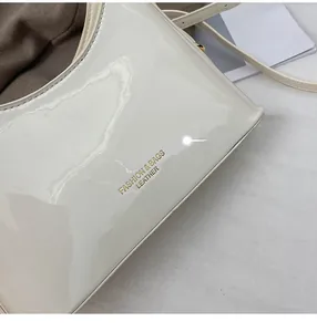 Detail view of creamy white patent leather bucket bag with gold fashion logo stamp