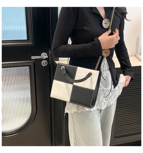 Detail of checkered pattern handbag with gold chain strap and black curved handle