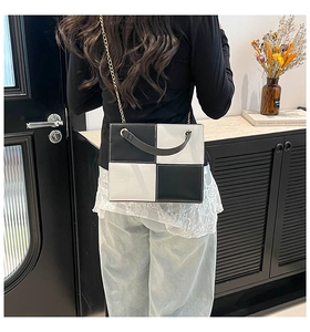Detail of a black and white checkerboard square bag with gold chain and glossy finish