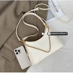 Close-up of a white hobo bag with gold chain and size reference next to a phone