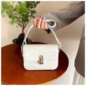Detail of white leather shoulder bag with gold metal clasp on a vintage wooden table