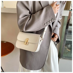 Close-up of creamy white crossbody bag with gold metal lock on a stylish grey blazer