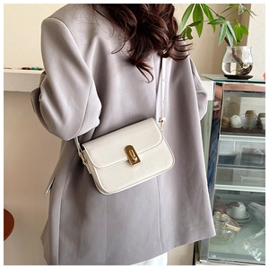 Detail of a minimalist cream-white crossbody bag with elegant gold metal oval lock buckle