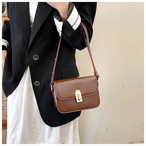 Detail of caramel leather crossbody bag featuring a gold oval twist lock and slim shoulder strap