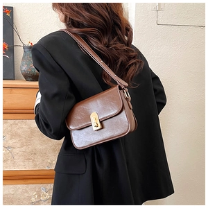 Close-up of retro brown shoulder bag with golden metallic clasp on a black blazer outfit
