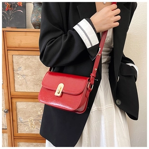 Detail of red glossy crossbody bag featuring a gold metal push-lock and shoulder strap