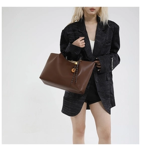 Detailed view of brown leather tote with wooden buckle and woven pendant detail
