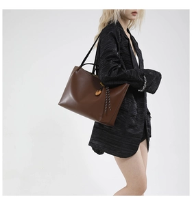 Deep brown leather tote bag with unique wood pendant and braided rope detail on shoulder