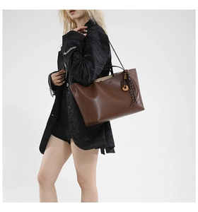 Close-up of brown leather tote bag featuring a woven rope charm and slim shoulder straps