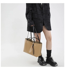 Detailed side view of khaki tote bag with black strap and decorative woven pendant on model