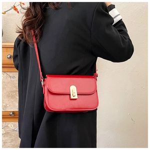 Detail of red leather crossbody bag with gold metal twist lock against black suit background