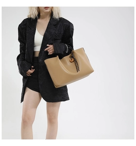 Detail view of large camel tote bag with braided charm on model in black suit