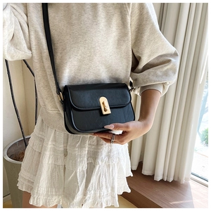 Detail of a black matte leather crossbody bag featuring a golden rectangular twist lock