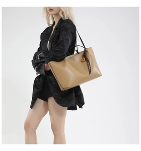 Detail of khaki leather tote bag with a wooden ring and woven rope pendant accessory