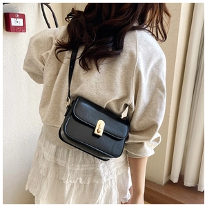 Model wearing a black square crossbody bag with a gold oval metal twist lock closure