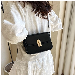 Detail of minimalist black leather crossbody bag with gold metal clasp on a model