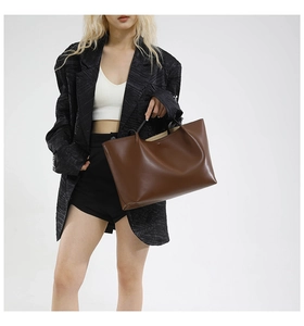 Side view of large brown leather tote bag worn by a model in a black textured blazer