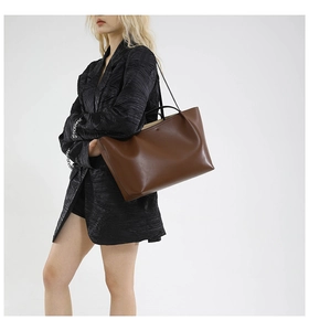 Minimalist dark brown leather tote bag displayed on model with shoulder strap and handle