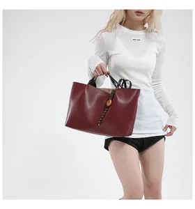 Detail of burgundy tote bag with black handles and woven rope pendant accessory