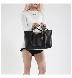 Close-up of large matte black leather tote bag with wooden charm and woven strap detail