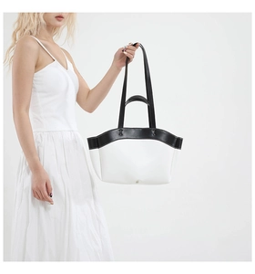 Detail of minimalist black and white tote bag showing contrast straps and metal closure